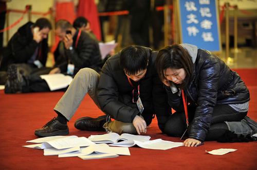 3月5日，第十一届全国人民代表大会第五次会议在北京人民大会堂开幕。这是记者跪在地上查阅刚刚领到的相关材料。新华社记者 王鹏 摄 