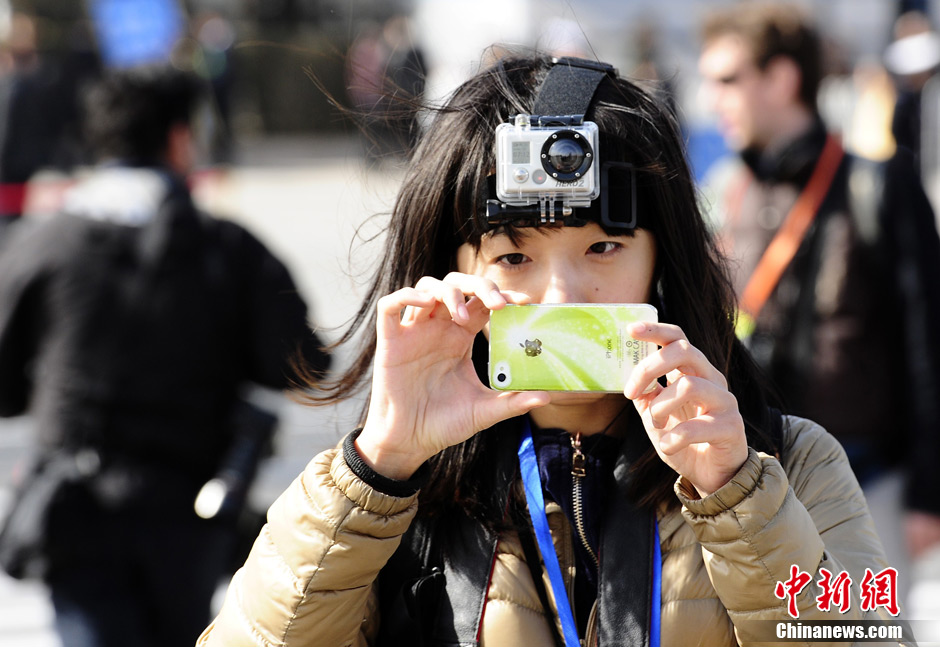 两会新闻大战，各媒体都派出“精兵强将”，为了捕捉一个瞬间，为了抢发一条稿件，早已“百炼成钢”的记者们使出浑身解数。图为3月3日，北京，全国政协十二届一次会议开幕。一名女记者头戴Hero摄像机，颈上挎着相机、手中拿着手机“全副武装”采访。中新社发 侯宇 摄
