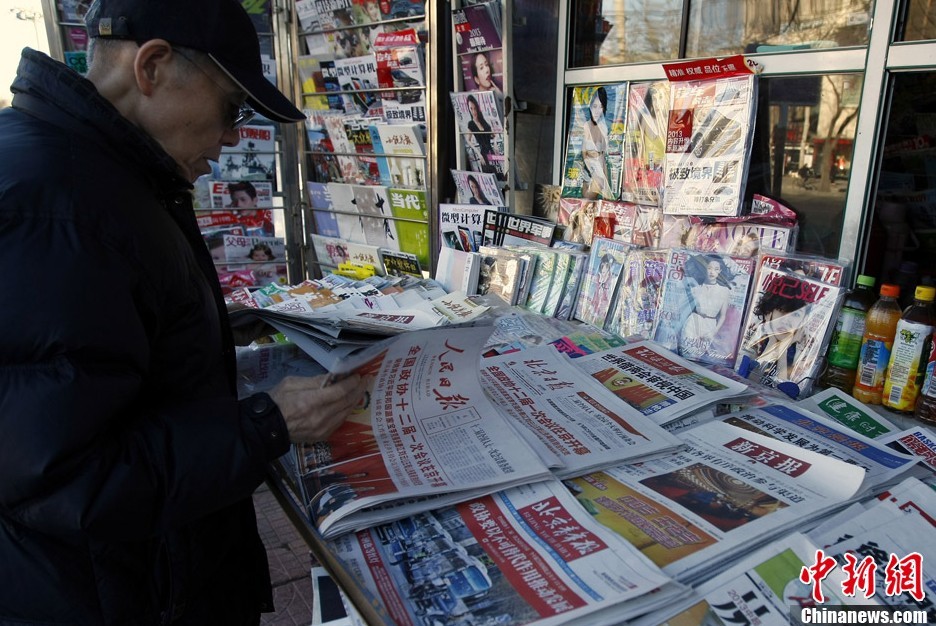 3月4日，一位北京市民在报摊翻阅当天报纸。当日，多家报纸的头版都报道了全国政协十二届一次会议开幕的消息。中新社发 李慧思 摄